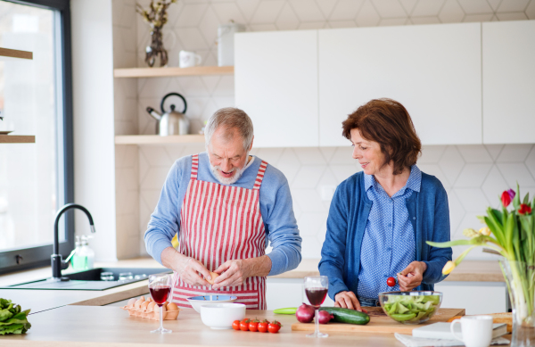 A portrait of happy senior couple indoors at home, cooking.