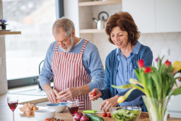 A portrait of happy senior couple in love indoors at home, cooking.