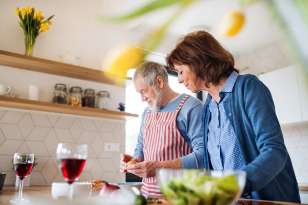 A portrait of happy senior couple in love indoors at home, cooking.