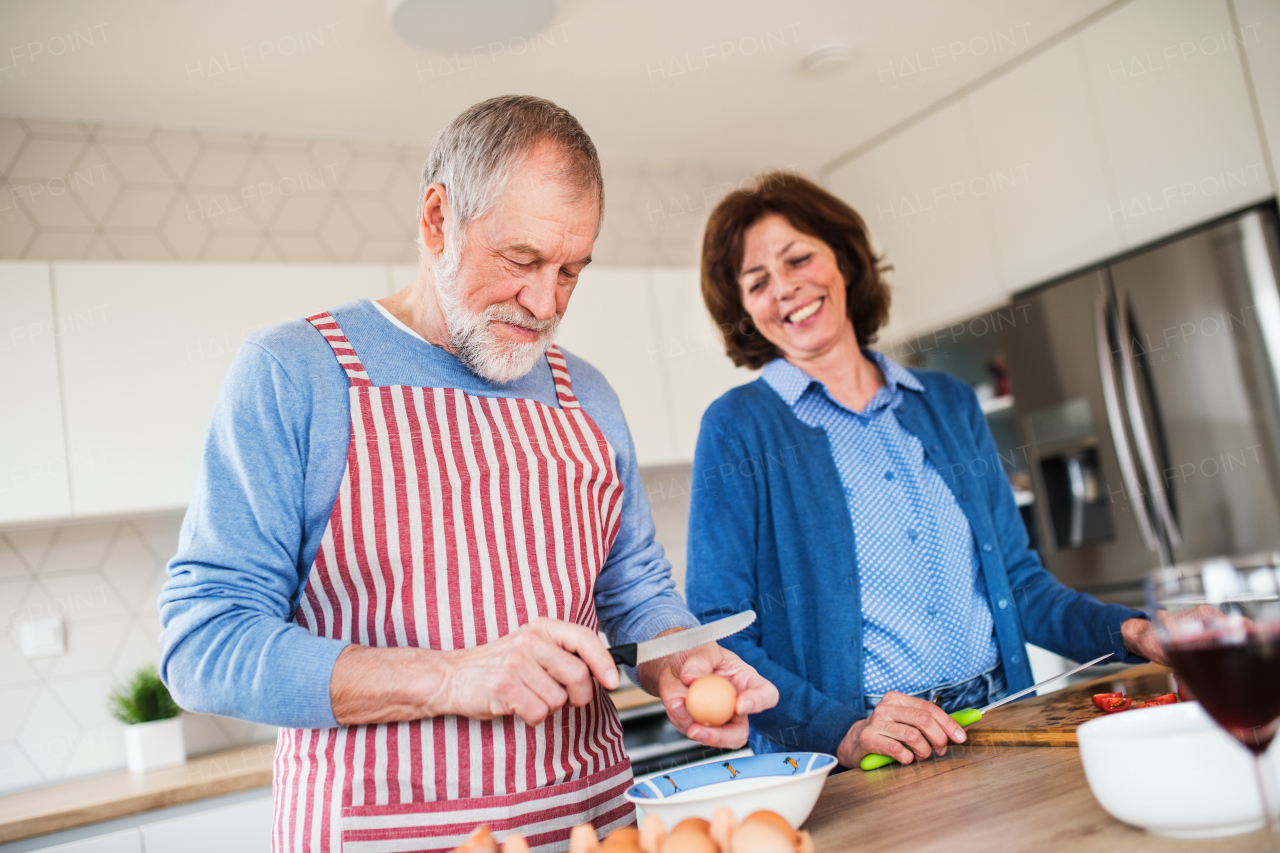 A portrait of happy senior couple in love indoors at home, cooking.