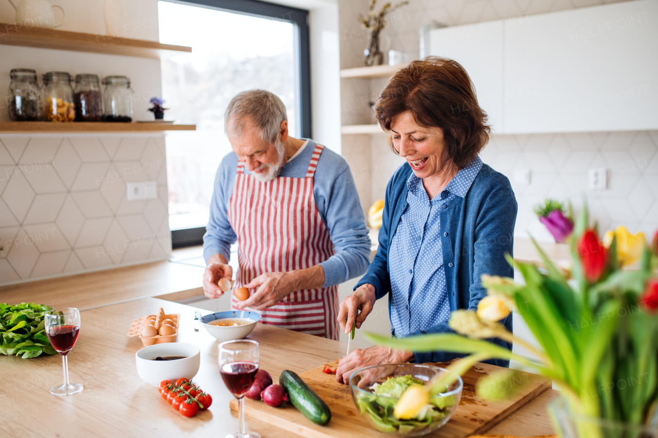 A portrait of happy senior couple in love indoors at home, cooking.