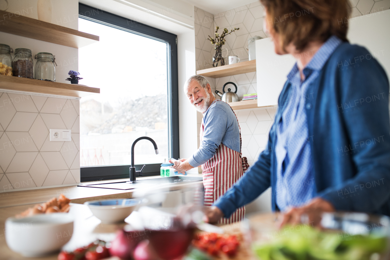 A portrait of happy senior couple indoors at home, cooking.