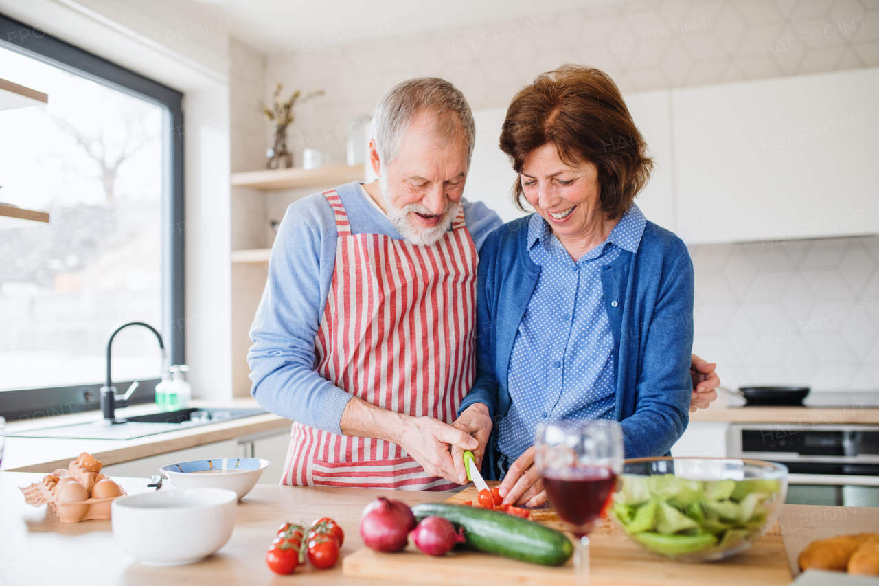 A portrait of happy senior couple in love indoors at home, cooking.