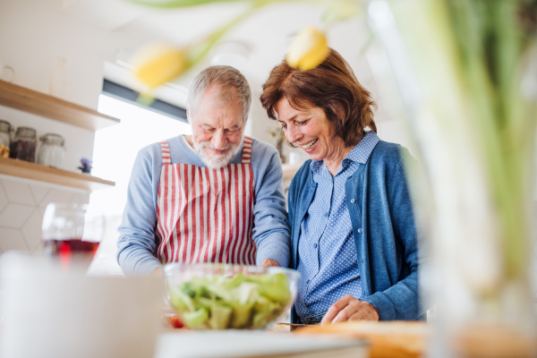 A portrait of happy senior couple in love indoors at home, cooking.