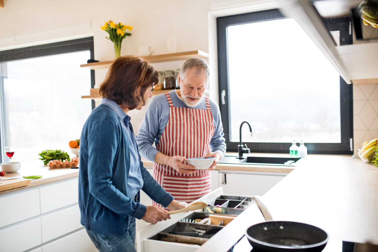 A portrait of happy senior couple in love indoors at home, cooking.