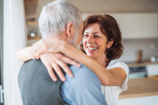 An affectionate senior couple in love standing indoors at home, hugging.