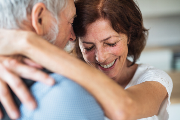 An affectionate senior couple in love standing indoors at home, hugging.