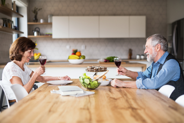 A senior couple in love having lunch indoors at home, talking.