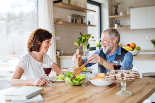 A senior couple in love having lunch indoors at home, talking.