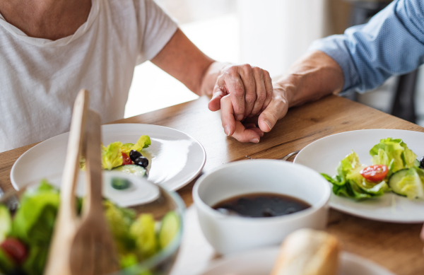 A midsection of senior couple in love indoors at home, holding hands when having lunch.