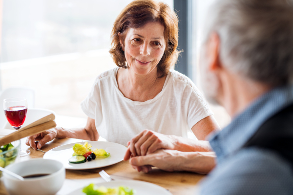 A senior couple in love having lunch indoors at home, holding hands.