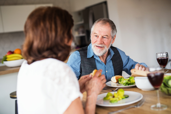 A senior couple in love having lunch indoors at home, talking.