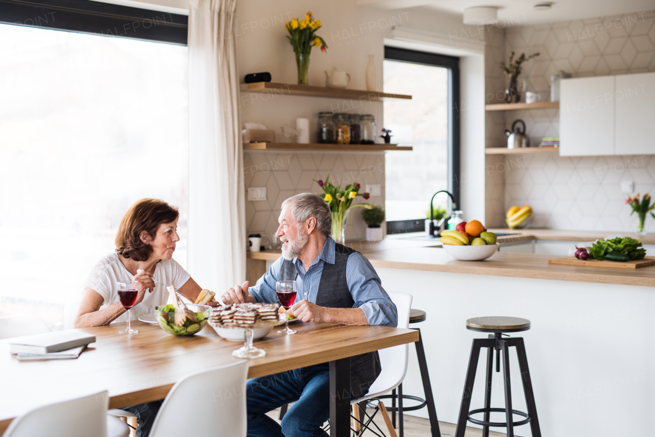 A senior couple in love having lunch indoors at home, talking.