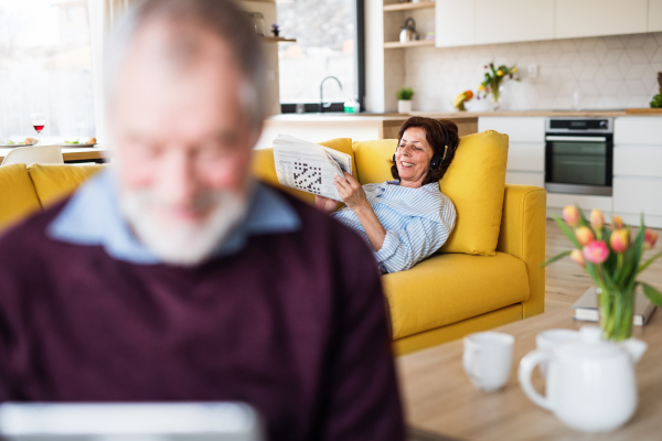 A senior couple with laptop and headpones indoors at home, relaxing.