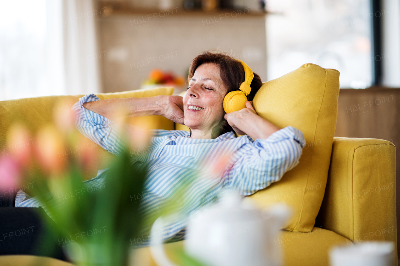 A senior woman with headphones and crosswords sitting on sofa indoors at home, resting.