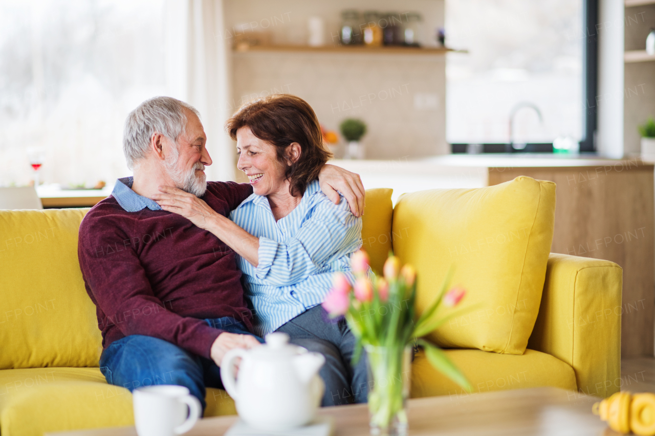 An affectionate senior couple in love sitting on sofa indoors at home, talking.