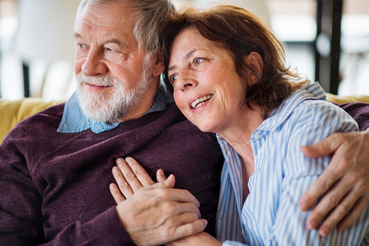 An affectionate senior couple in love sitting on sofa indoors at home, talking.