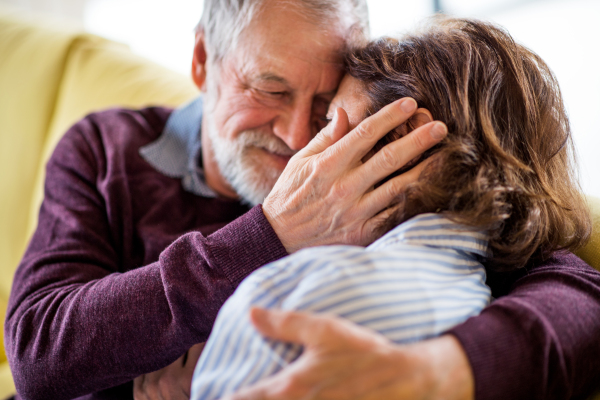 An affectionate senior couple in love sitting on sofa indoors at home, hugging.