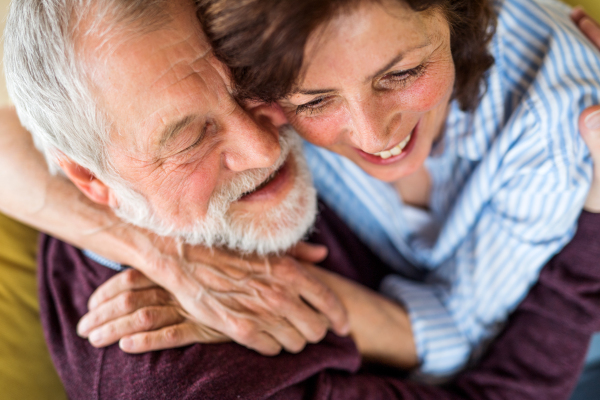 A top view of affectionate senior couple in love sitting on sofa indoors at home, hugging.