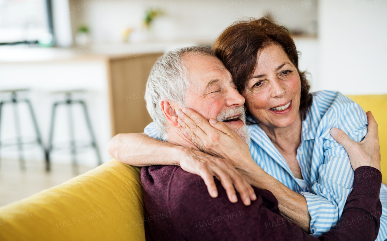 An affectionate senior couple in love sitting on sofa indoors at home, talking.