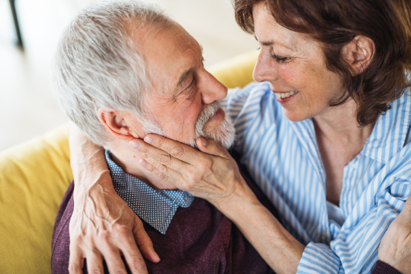 An affectionate senior couple in love sitting on sofa indoors at home, talking.