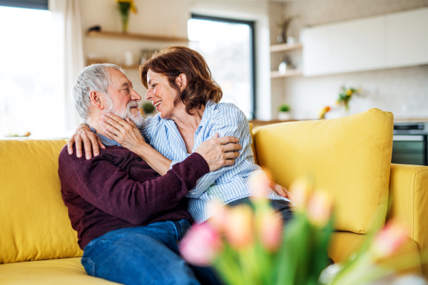 An affectionate senior couple in love sitting on sofa indoors at home, talking.