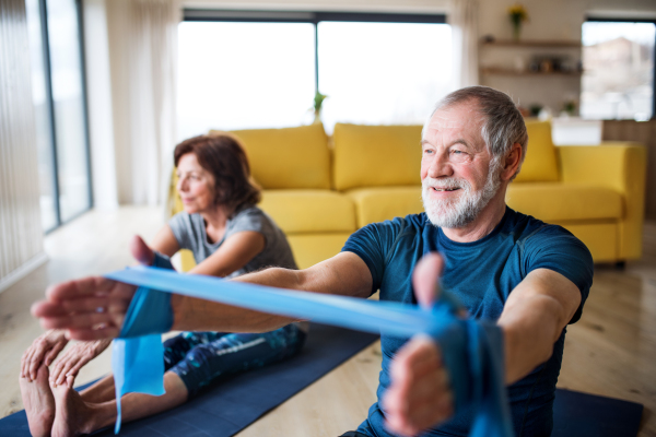 A happy senior couple with elastic bands indoors at home, doing exercise on the floor.