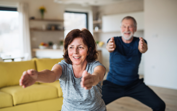 A happy senior couple indoors at home, doing exercise indoors.