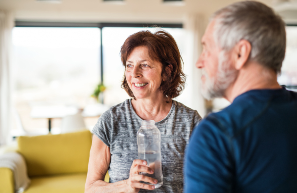 A happy senior couple indoors at home, resting after doing exercise indoors.