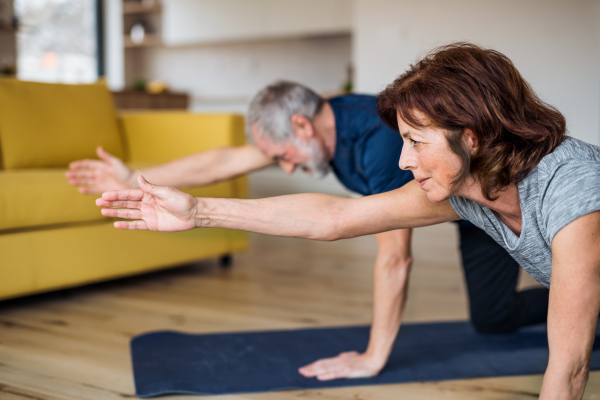 A happy senior couple indoors at home, doing exercise on the floor.