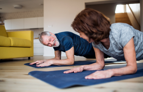 A happy senior couple indoors at home, doing exercise on the floor.