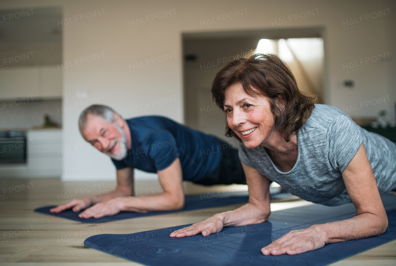 A happy senior couple indoors at home, doing exercise on the floor.