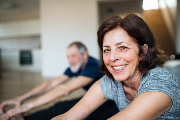 A happy senior couple indoors at home, doing exercise on the floor.