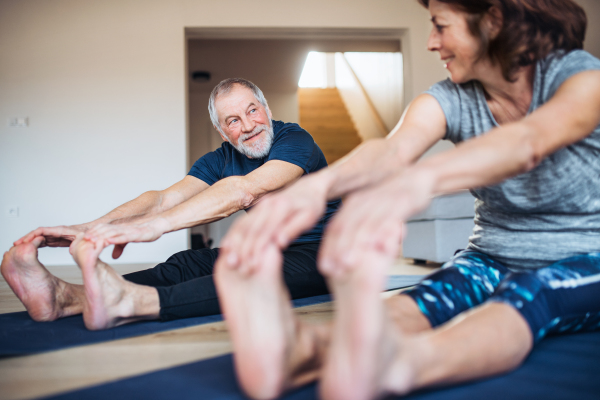 A happy senior couple indoors at home, doing exercise on the floor.