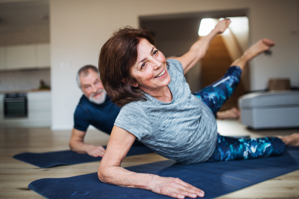 A happy senior couple indoors at home, doing exercise on the floor.