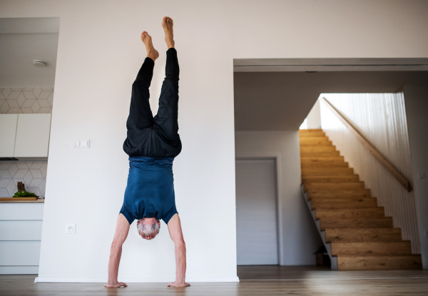 A senior man indoors at home, doing handstand exercise indoors. Copy space.