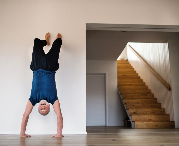 A senior man indoors at home, doing handstand exercise indoors. Copy space.