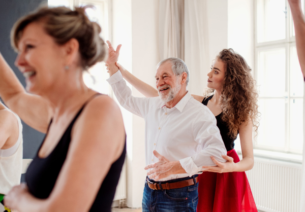 A group of senior people attending dancing class with dance teacher.