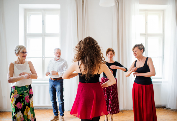 A group of senior people attending dancing class with dance teacher.