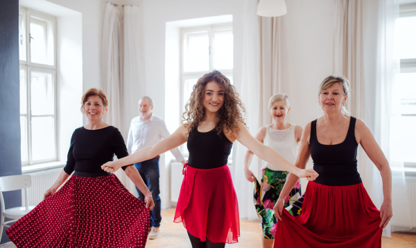 A group of senior people attending dancing class with dance teacher.