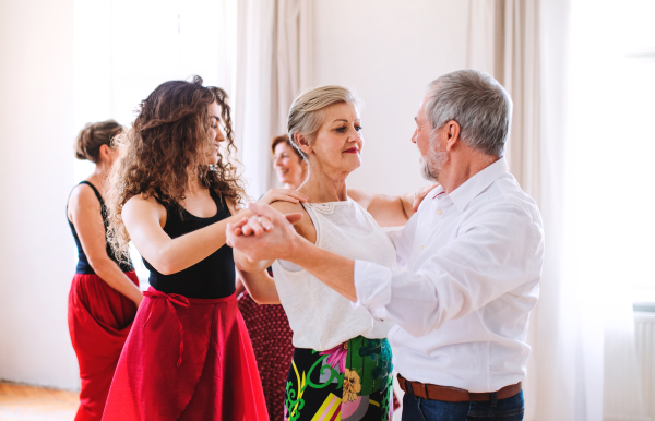 A group of senior people attending dancing class with dance teacher.