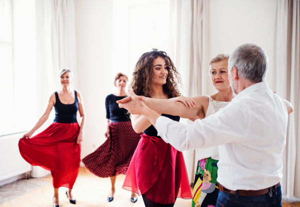 A group of senior people attending dancing class with young dance teacher.