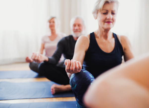 Group of active senior people doing yoga exercise in community center club.