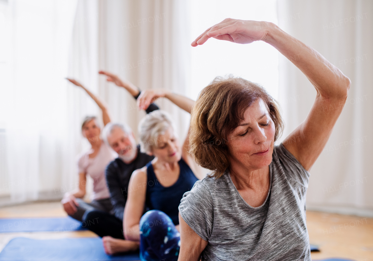 Group of active senior people doing yoga exercise in community center club.