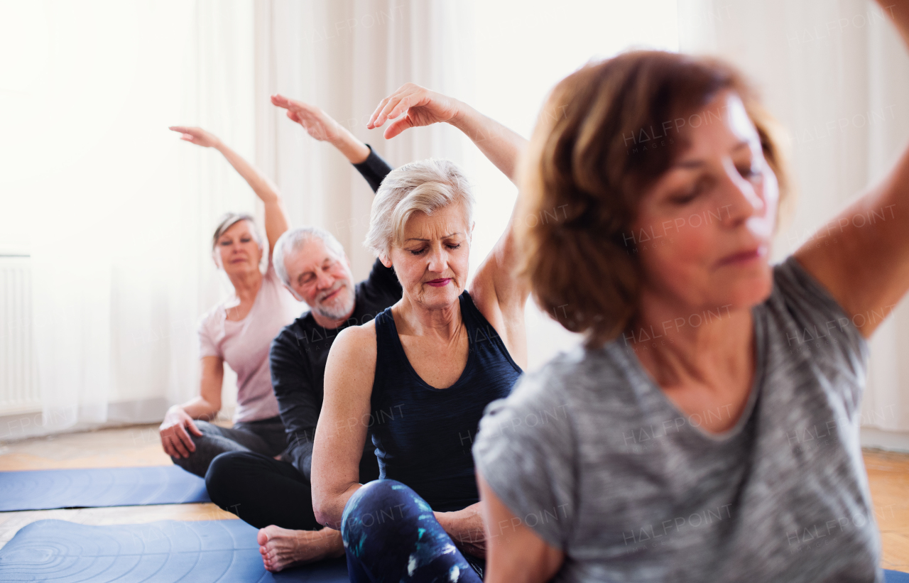 Group of active senior people doing yoga exercise in community center club.