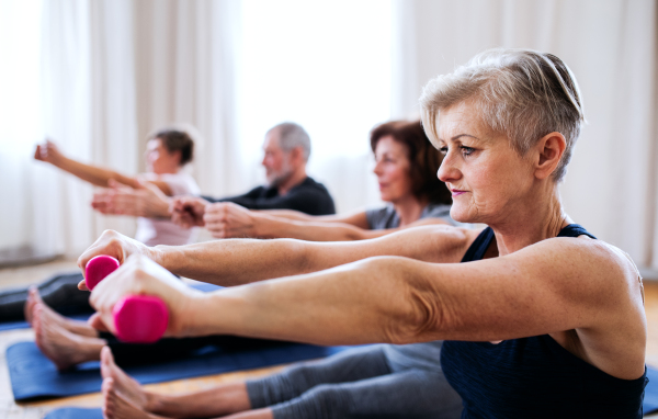 A group of active senior people doing exercise with dumbbells in community center club.