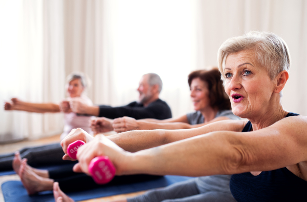 Group of active senior people doing exercise with dumbbells in community center club.