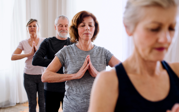 Group of active senior people doing yoga exercise in community center club.