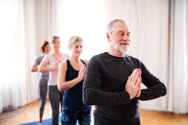 Group of active senior people doing yoga exercise in community center club.