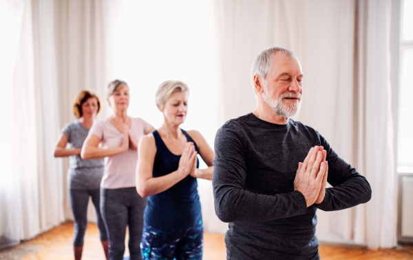 Group of active senior people doing yoga exercise in community center club.